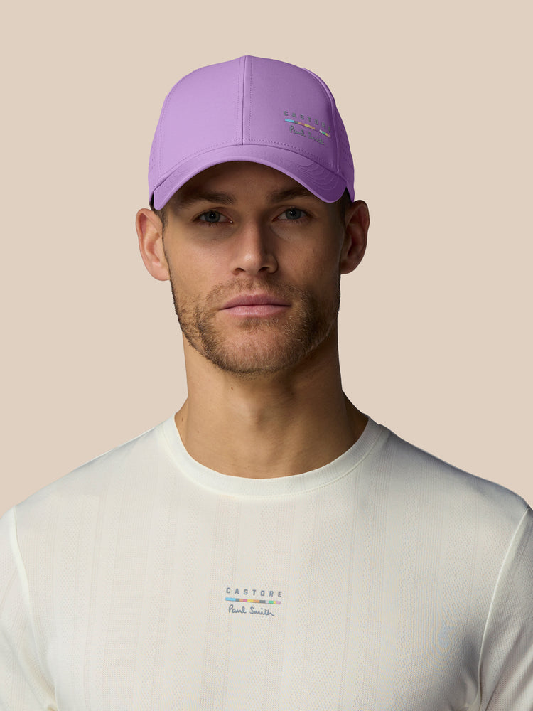 Man wearing a purple cap and white shirt with brand logos on a beige background