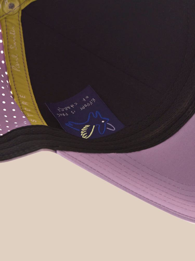 Close-up of a purple and black cap with a logo on a beige background