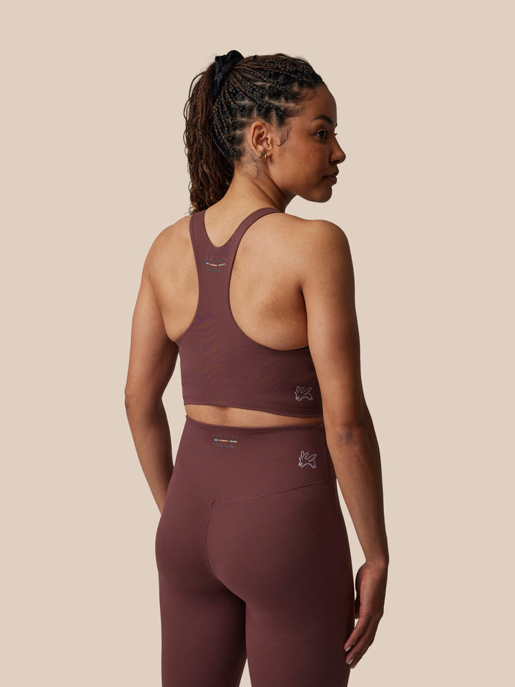 Woman wearing a maroon sports bra and leggings set on a beige background