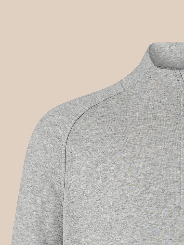 Close-up of a light gray heathered quarter-zip pullover sweater showing the shoulder seam and collar, set against a solid beige background.