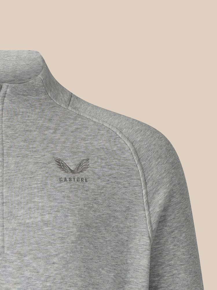 Close-up of a heather gray quarter-zip pullover sweatshirt with a small embroidered winged logo and the word 'CASTORE' on the left chest, set against a solid beige background.