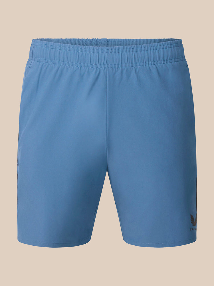Light blue athletic shorts with an elastic waistband and a small black Castore logo on the lower left hem, shown against a solid beige background.