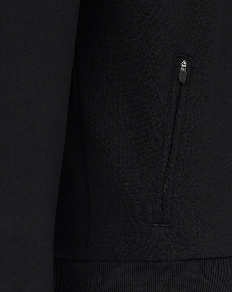 Close-up of a black hoodie with a brand logo on the chest pocket against a dark background.