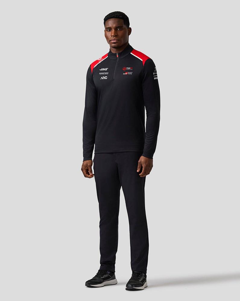 Person wearing a black tracksuit with red accents on a gray background